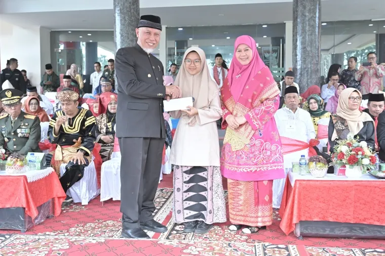 Gubernur Mahyeldi memberi hadiah khusus pada Atila Rahadatul Ilmi, siswi kelas XI SMA Negeri 10 Padang tampil memukau saat membacakan Undang-Undang Dasar 1945 tanpa melihat teks, di halaman Kantor Gubernur Sumatera Barat (Sumbar), Jumat (2/5/2025). Foto: